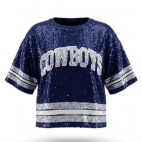A navy blue sequined short-sleeve sweatshirt featuring "COWBOYS" in white and silver lettered appliqué across the chest, with matching silver sequined stripes on the sleeves and hem.