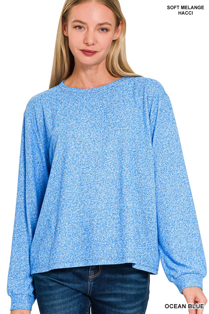 A woman wearing an ocean blue soft melange sweatshirt with long sleeves and a relaxed, slightly oversized fit, paired with dark denim jeans.
