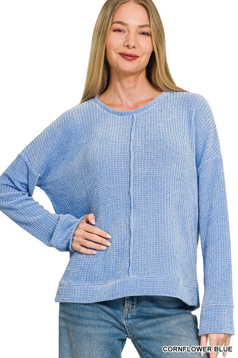 A woman wearing a cornflower blue ribbed long-sleeve top with a crew neckline and vertical seam detail down the front, paired with blue jeans.