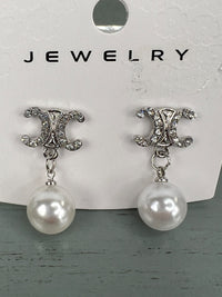 Pair of silver-tone drop earrings featuring ornate CC-shaped studs embellished with crystals, each suspending a white pearl. The earrings are displayed on a white jewelry card.
