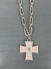 A silver-toned chain necklace featuring oval link segments, suspending a rectangular cross pendant with decorative dot details and a central oval medallion, displayed on a gray wooden background.