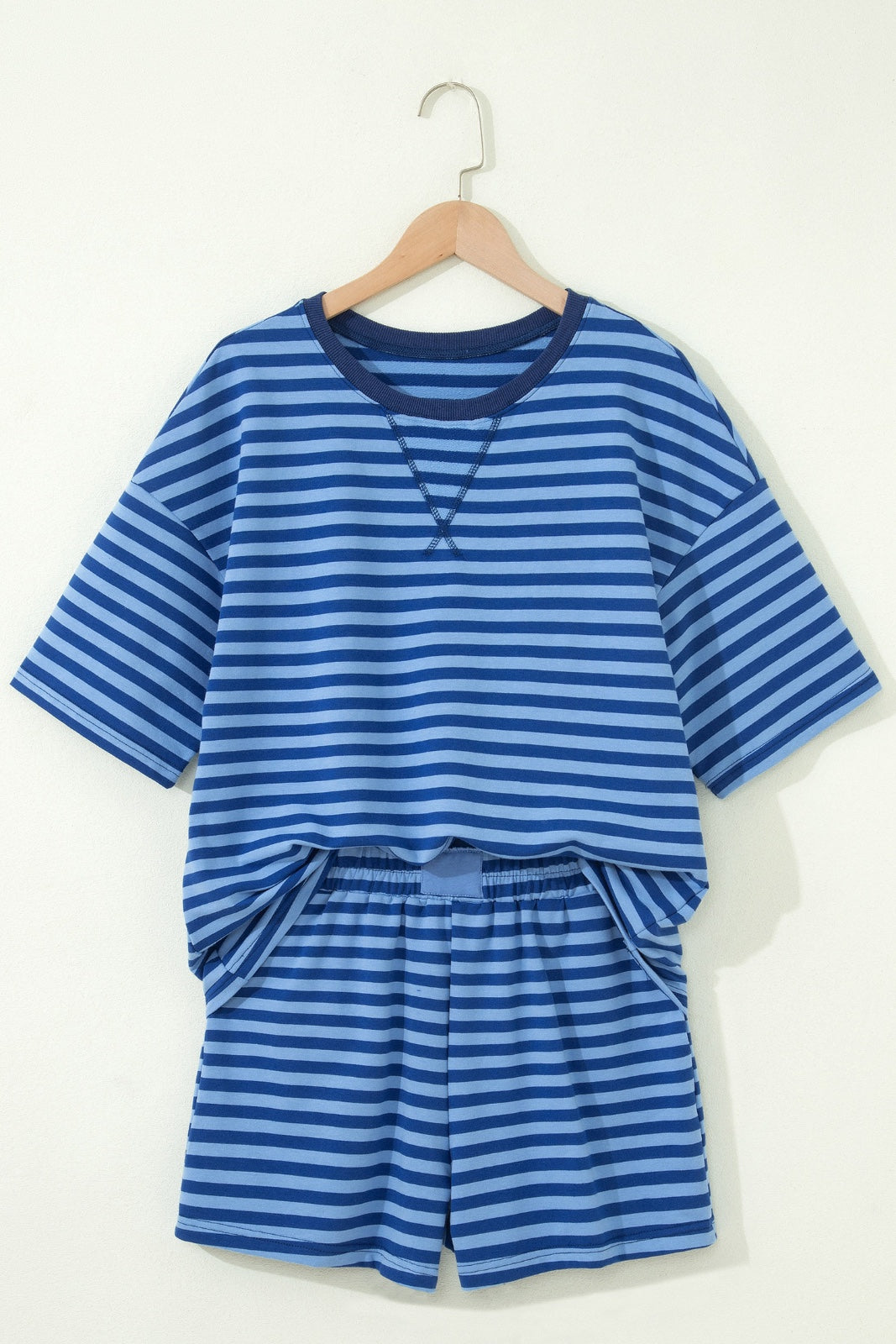 A children's two-piece set featuring a blue and light blue striped short-sleeved shirt with a crew neckline, paired with matching striped shorts with an elastic waistband, displayed on a wooden hanger against a cream background.