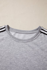 A light gray crewneck t-shirt with black and white striped trim on the short sleeves, displayed flat against a beige background.