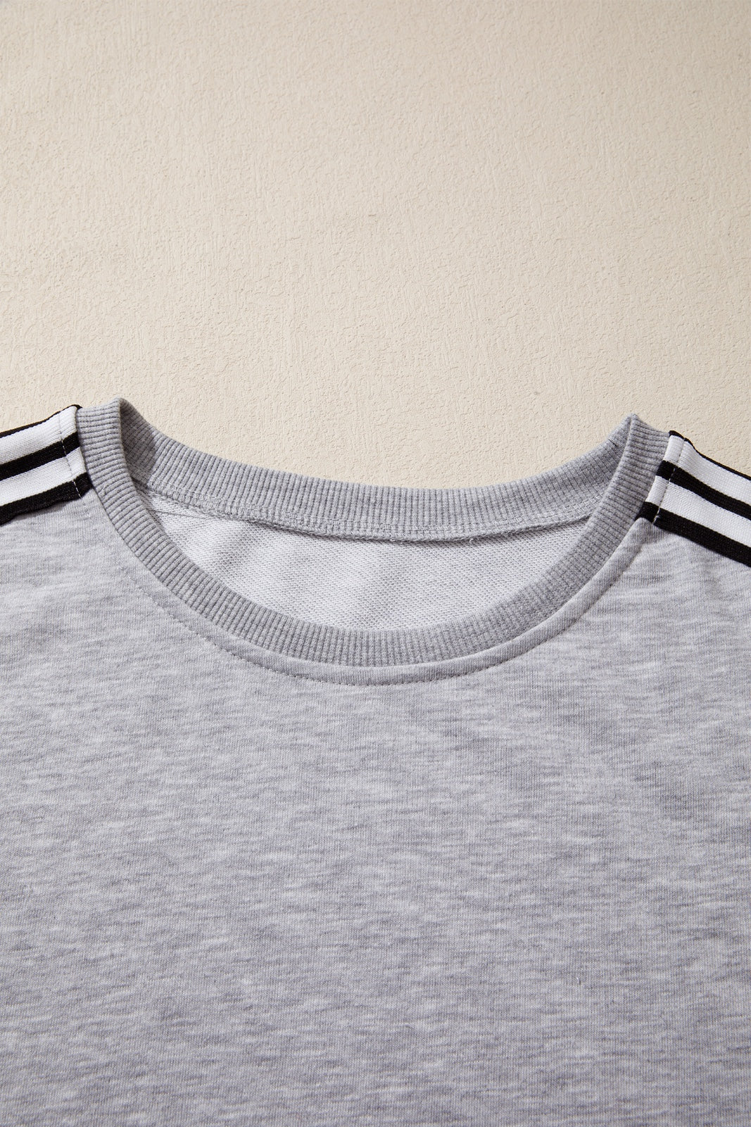 A light gray crewneck t-shirt with black and white striped trim on the short sleeves, displayed flat against a beige background.