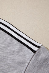 Close-up of a light gray long-sleeve shirt featuring white and black striped trim on the cuffs, laid flat against a beige background.