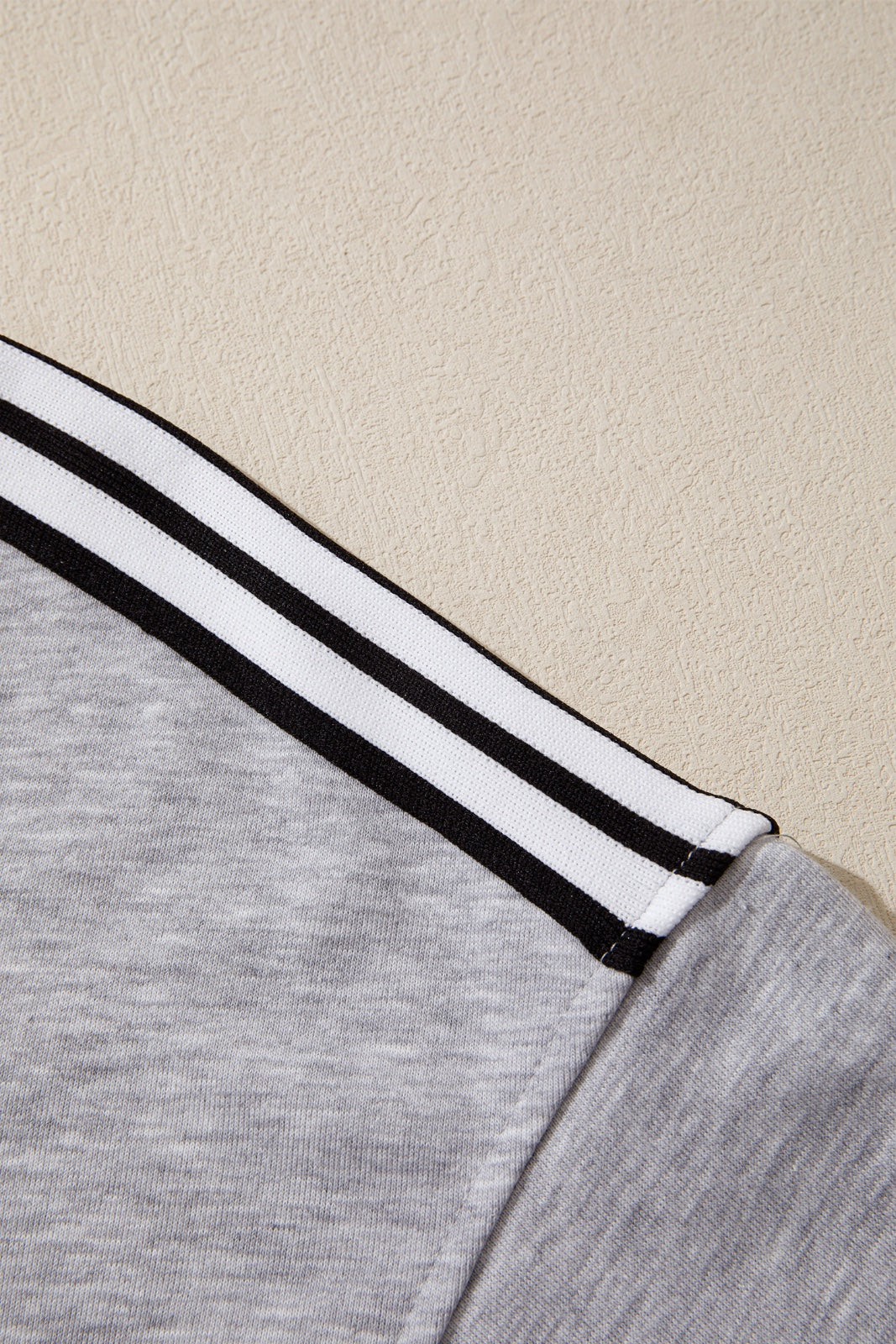 Close-up of a light gray long-sleeve shirt featuring white and black striped trim on the cuffs, laid flat against a beige background.
