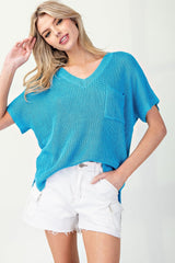 A woman wearing a bright turquoise ribbed short-sleeve V-neck sweater paired with white distressed denim shorts, posed against a neutral background.