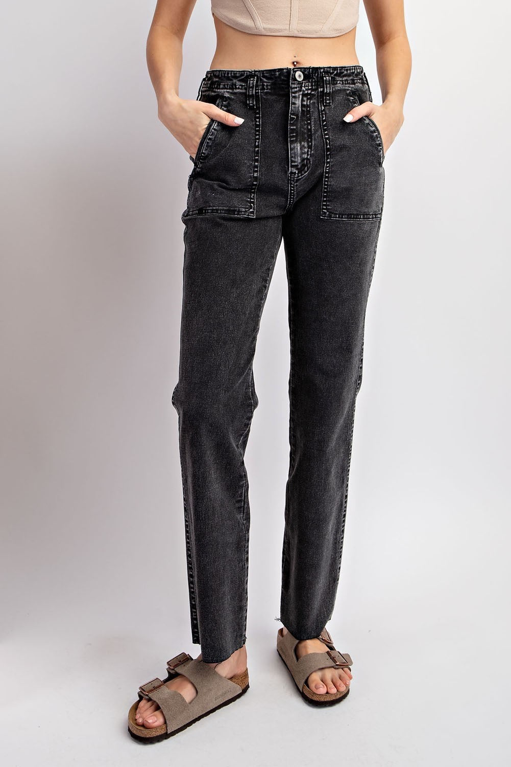 Black acid-wash straight-leg jeans with cargo pockets and a high waist, styled with a beige crop top and brown slide sandals.