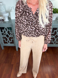 A woman wearing a burgundy floral print blouse with long sleeves paired with cream-colored ribbed knit joggers featuring a drawstring waist.