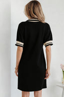 A woman viewed from behind wearing a black short-sleeve dress with cream and black striped trim at the neckline and cuffs, featuring a simple A-line silhouette.