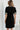 A woman viewed from behind wearing a black short-sleeve dress with cream and black striped trim at the neckline and cuffs, featuring a simple A-line silhouette.