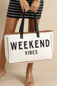 A person wearing a black and white striped dress holds a large cream canvas tote bag with "WEEKEND VIBES" text printed in black and tan leather trim, featuring black handles.