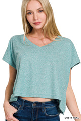 A woman wearing a dusty teal heathered short-sleeve v-neck t-shirt with a cropped, relaxed fit, paired with dark denim jeans.
