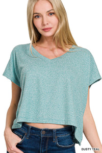 A woman wearing a dusty teal heathered short-sleeve v-neck t-shirt with a cropped, relaxed fit, paired with dark denim jeans.