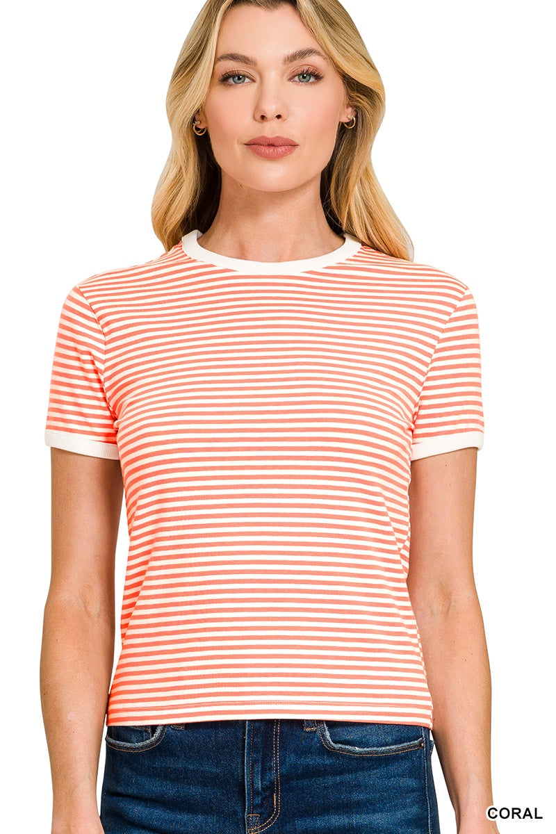 A woman wearing a coral and white striped short-sleeve crew neck t-shirt paired with dark denim jeans, standing against a white background.