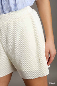 A cream-colored ribbed knit shorts with an elastic waistband, paired with a light blue textured top. The shorts feature vertical ribbed detailing and fall to mid-thigh length.