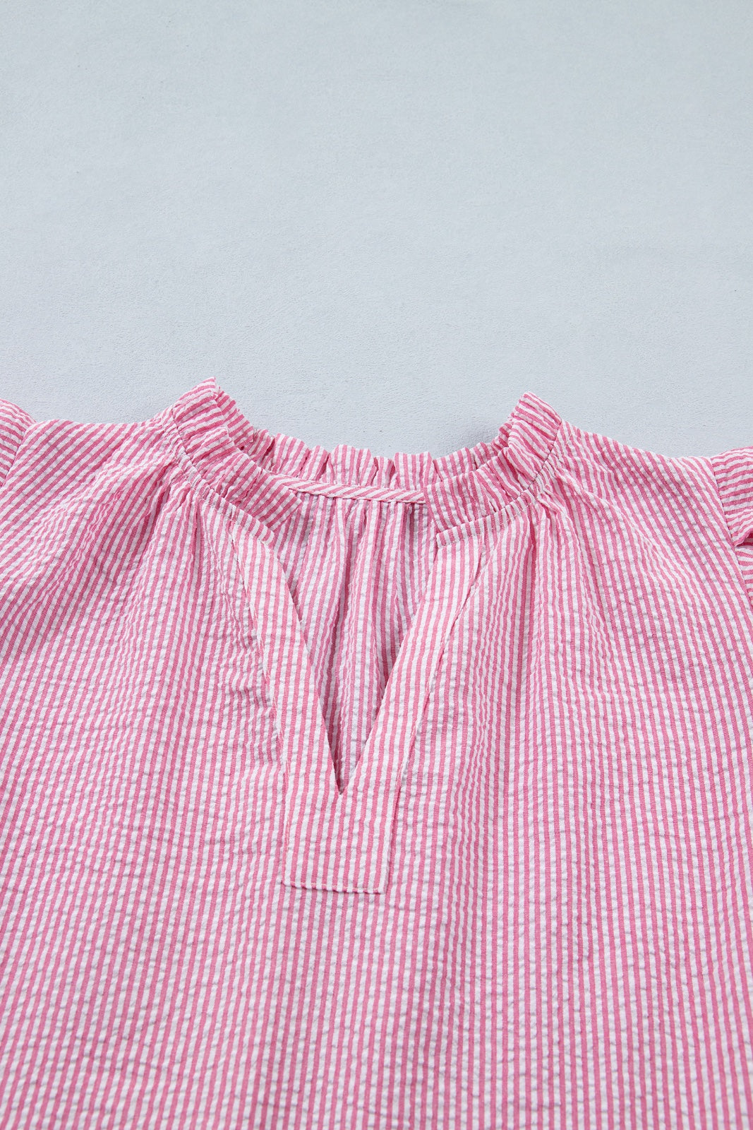 A pink and white striped off-shoulder top with a ruffled neckline and short puffed sleeves, displayed flat against a light gray background.