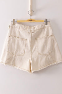 Cream-colored denim shorts with a high waist, displayed on a wooden hanger. The shorts feature visible stitching, dual back pockets, and frayed hem edges.