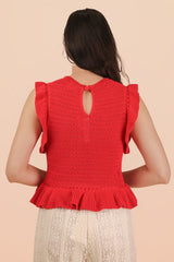 A woman wearing a bright red sleeveless knit top with ruffled flutter sleeves and a keyhole cutout on the back, paired with a cream-colored lace skirt.