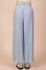A light blue wide-leg pair of pants with an elastic waistband and relaxed fit, paired with metallic silver platform shoes against a neutral beige background.