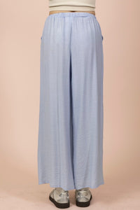 A light blue wide-leg pair of pants with an elastic waistband and relaxed fit, paired with metallic silver platform shoes against a neutral beige background.