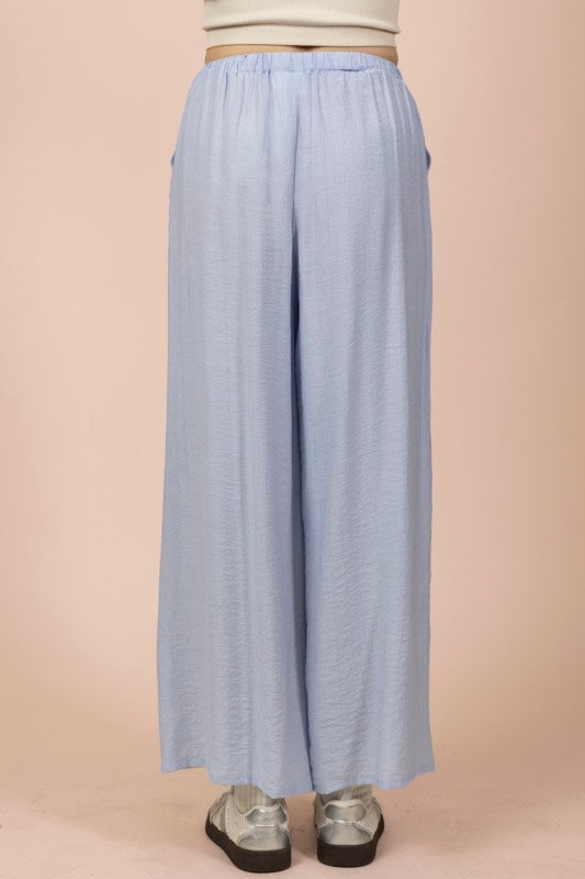 A light blue wide-leg pair of pants with an elastic waistband and relaxed fit, paired with metallic silver platform shoes against a neutral beige background.