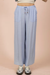 Light blue wide-leg pants with an elastic drawstring waist, front pockets, and a relaxed fit, styled with a cream crop top and platform sneakers against a beige background.