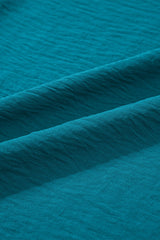 Close-up of a teal blue textured fabric with subtle horizontal ribbing and diagonal folds, showing the soft, matte finish and drape of the material.