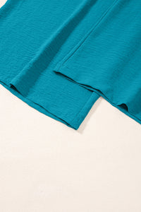 Turquoise blue linen fabric with rolled hems and natural texture, displayed flat against a white background showing the garment's drape and construction details.