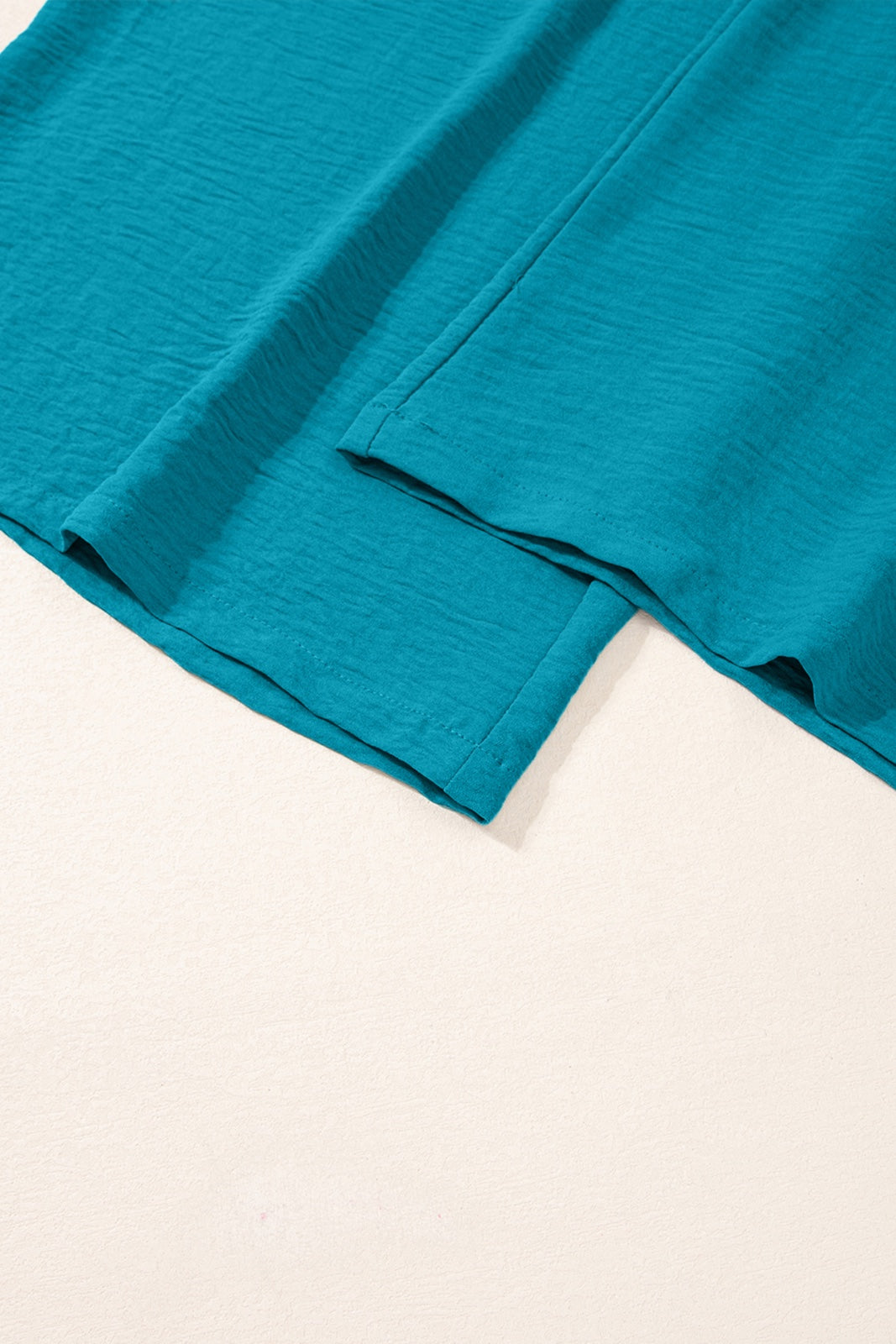 Turquoise blue linen fabric with rolled hems and natural texture, displayed flat against a white background showing the garment's drape and construction details.