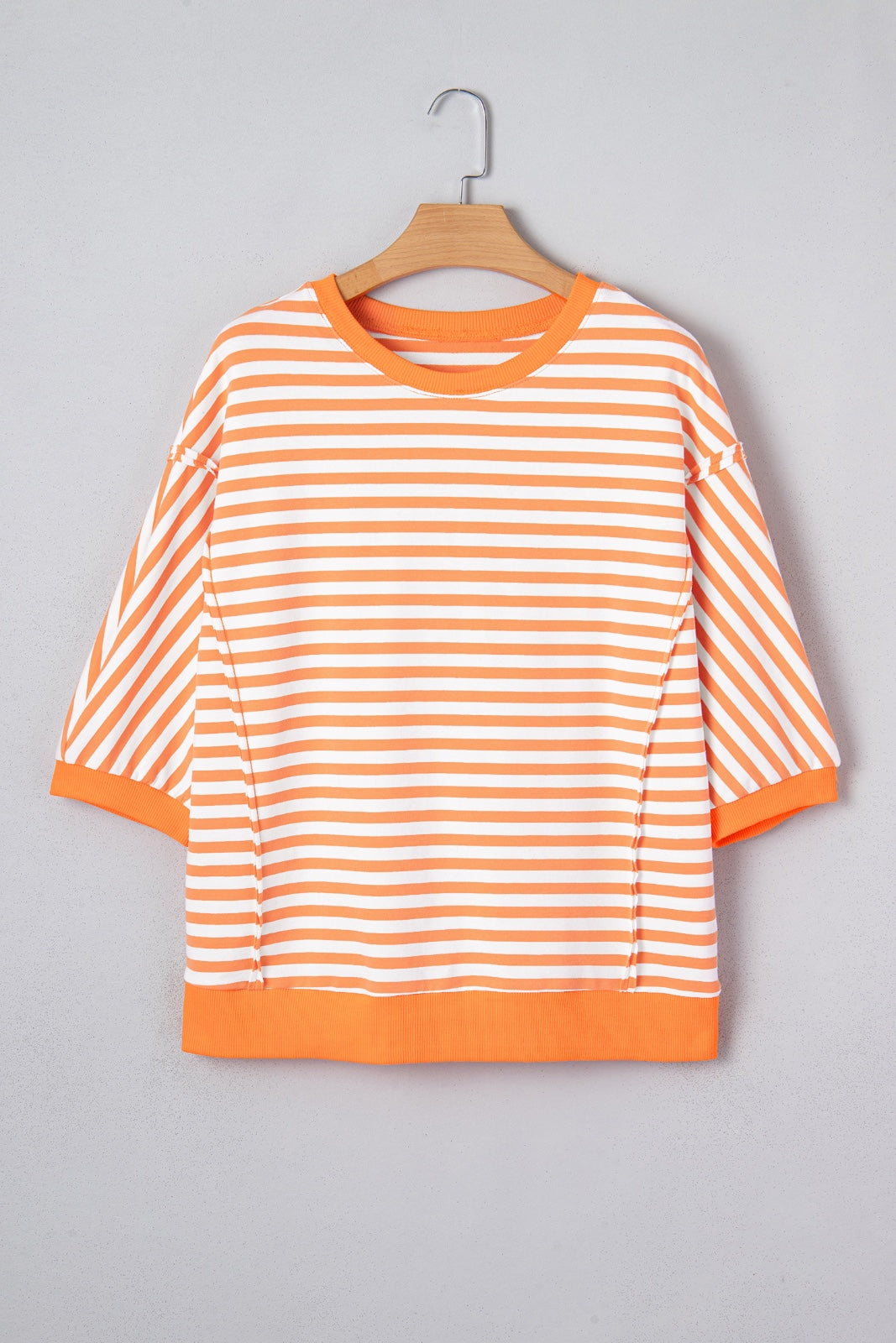 A bright orange and white striped short-sleeve sweatshirt displayed on a wooden hanger against a gray background. The garment features horizontal stripes throughout, ribbed cuffs and hem, and a classic crew neckline.