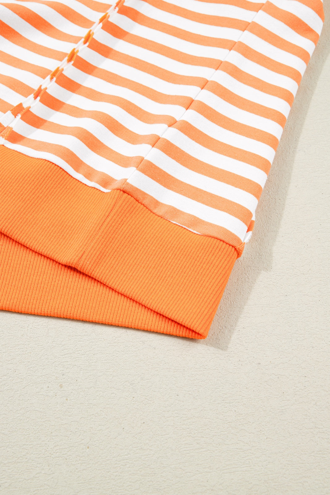 Close-up of an orange and white striped short-sleeve shirt with ribbed orange trim at the cuffs and hem, displayed flat on a neutral background.