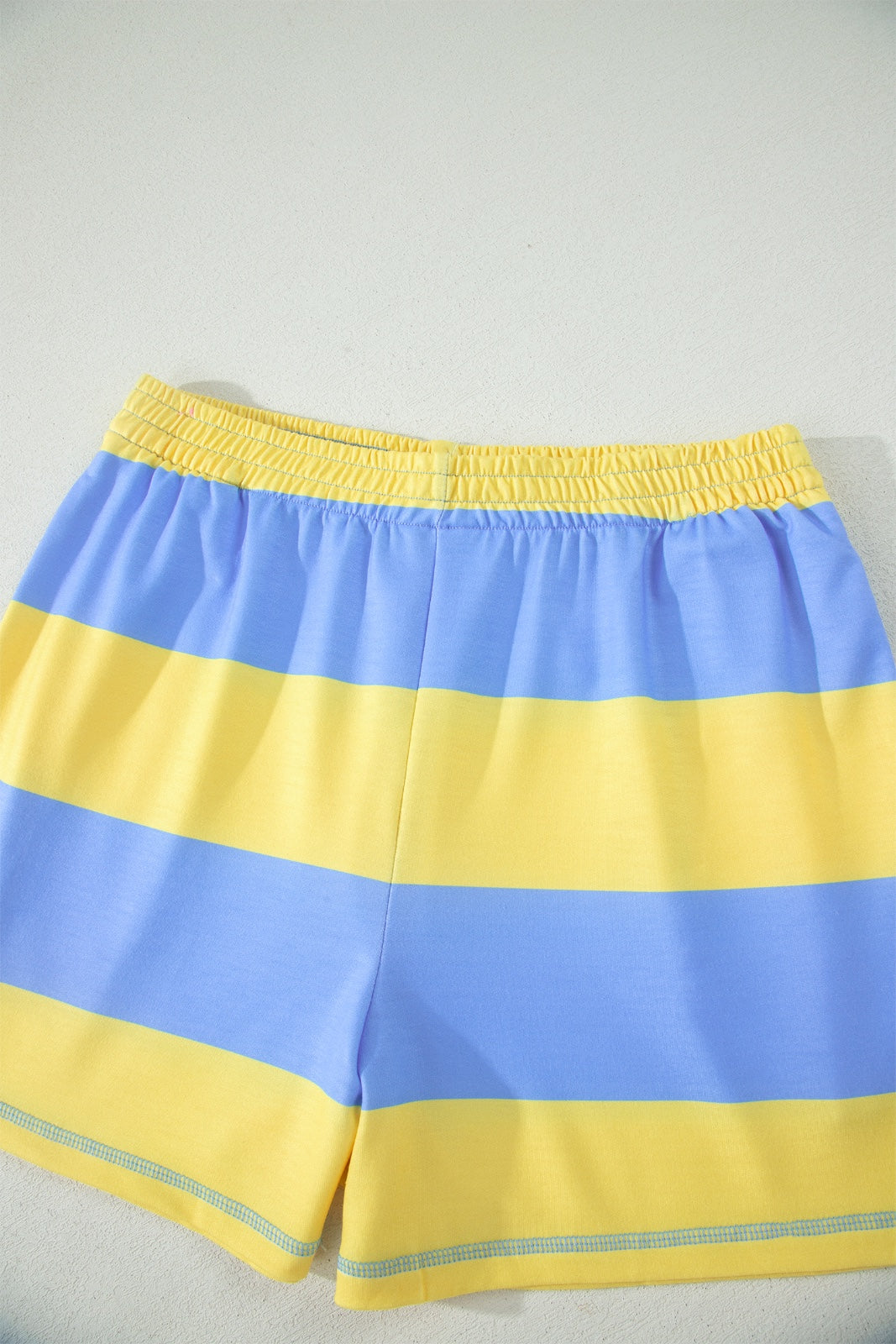 Blue and yellow striped swim shorts with an elastic waistband and reflective trim at the hem. The shorts feature horizontal color-blocking with alternating blue and yellow stripes throughout.