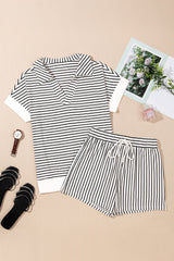 A black and white striped short-sleeve t-shirt and matching striped shorts set laid flat on a beige background, styled with black sandals, a watch, and decorative accessories including photos and a perfume bottle.