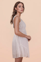 A woman wearing a light lavender sleeveless dress with a gathered waist and textured fabric, featuring delicate ruffled straps and a knee-length A-line silhouette against a neutral beige background.