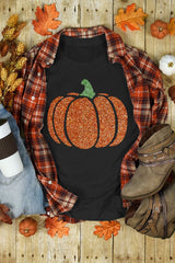 Black sleeveless tank top featuring a glittery orange pumpkin with a green stem, displayed flat lay with a plaid flannel shirt, autumn leaves, small pumpkins, boots, and fall decorations on a wooden background.