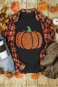 Black sleeveless tank top featuring a glittery orange pumpkin with a green stem, displayed flat lay with a plaid flannel shirt, autumn leaves, small pumpkins, boots, and fall decorations on a wooden background.