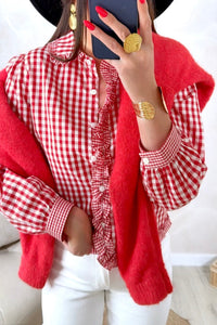 A red and white gingham check blouse with ruffled front placket and voluminous sleeves, paired with a solid red cardigan. The outfit is styled with gold circular earrings and red nail polish.