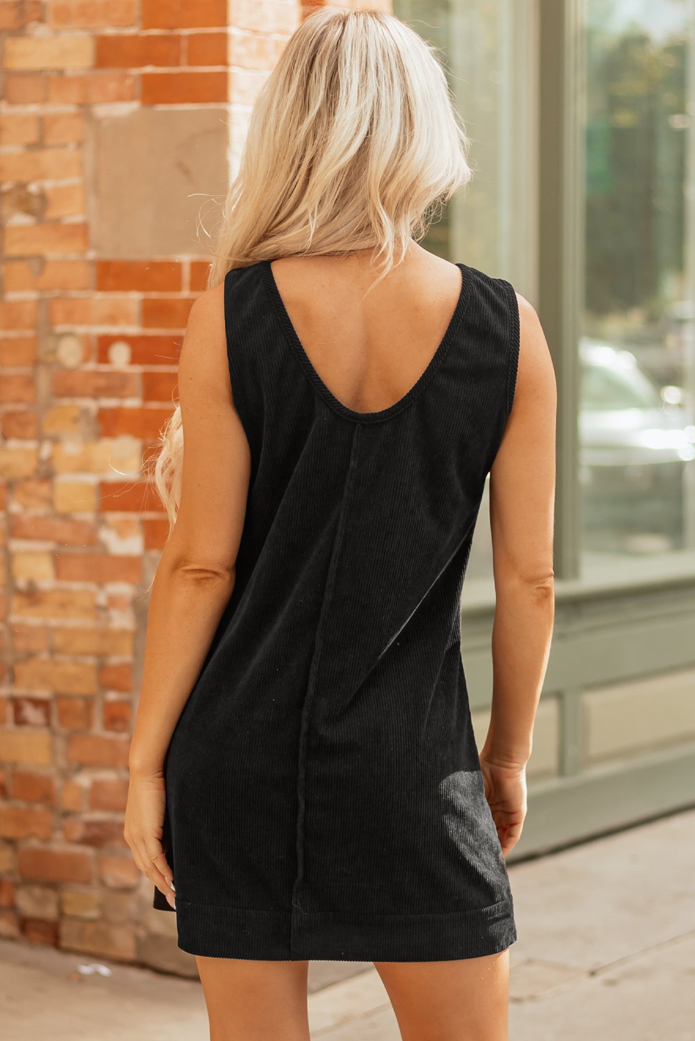 A sleeveless black ribbed knit dress hanging on a wooden hanger against a white background. The dress features a simple A-line silhouette with a round neckline and a vertical center seam detail.
