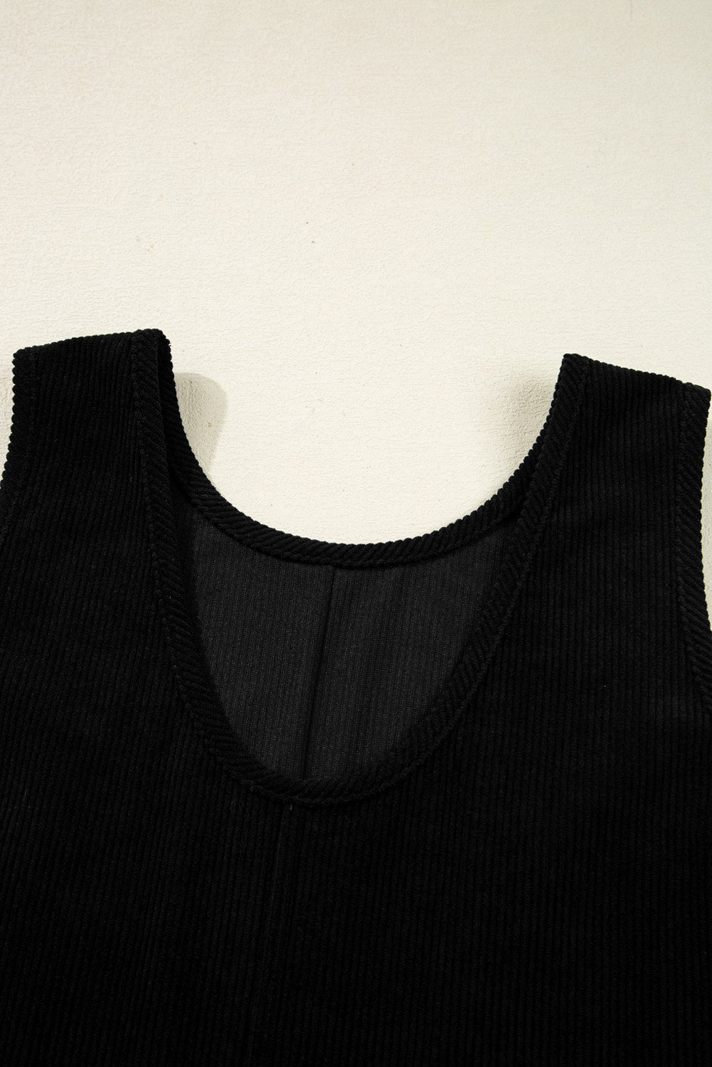 Black ribbed sleeveless tank top displayed flat against a cream background, showing the round neckline and textured knit fabric detail.