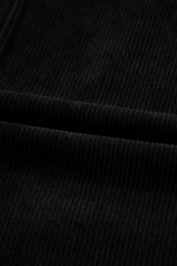 Close-up of black ribbed knit fabric showing vertical texture and subtle folds in the material. The garment features a classic ribbed knit pattern in solid black.