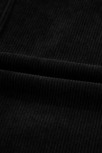 Close-up of black ribbed knit fabric showing vertical texture and subtle folds in the material. The garment features a classic ribbed knit pattern in solid black.