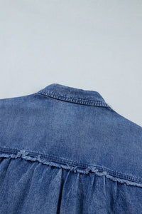 Close-up of a blue denim garment showing the back yoke and upper back panel with visible stitching and a ruched or gathered detail along the lower edge.