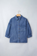 A blue denim button-up shirt displayed on a wooden hanger against a white background, featuring a classic collar, chest pocket, and three-quarter length sleeves with rolled cuffs.