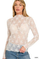 A woman models an ivory long-sleeve lace top with delicate white floral embroidery throughout. The sheer blouse features a mock neck and fitted silhouette, paired with blue denim jeans.