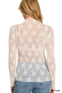 Rear view of an ivory lace long-sleeve crop top featuring an all-over white floral embroidered pattern on sheer mesh fabric, worn over a light blue denim.