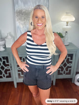 A woman wearing a navy and white striped sleeveless tank top paired with dark denim shorts with cargo pockets, standing indoors with hands on hips.