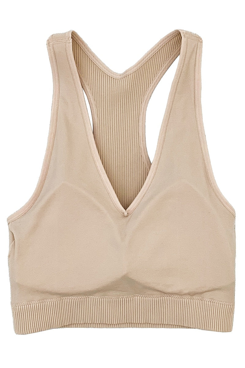 A beige racerback sports bra with a deep V-neckline and ribbed knit detailing on the back and lower band. The bra features a seamless front design and supportive structure in a neutral tan color.
