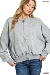 A woman wearing an acid wash gray zip-up bomber jacket with ribbed collar and cuffs, paired with dark blue jeans. The jacket features a relaxed fit with contrast stitching details across the front.