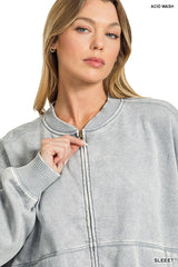 A woman wearing a light gray acid wash zip-up sweatshirt with ribbed collar and cuffs, featuring a drawstring at the neckline.